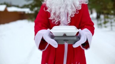 Noel Baba 'nın ellerinde karlı havada yiyecek dağıtım konteynırları. Noel arifesi terfisi. Hazır sıcak sipariş, tek kullanımlık plastik kutu. Yeni yıl yemekleri. Uzayı kopyala, taklit et