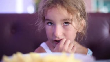 5 yaşındaki bir kız, kafeteryada patates kızartması yerken, ellerini çiğnerken ve surat yaparken komiktir.