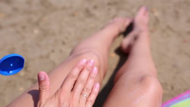 ビーチの女性はオレンジのチューブから日焼け止めローションで彼女の足を磨きます スキンケア Uv保護 日焼け止め ビーチの休日 — ストック動画