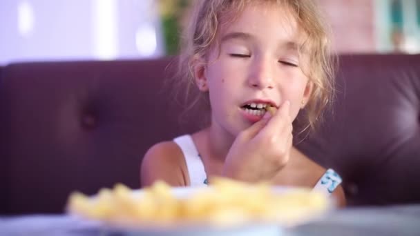 一个5岁的女孩在咖啡店里用手吃薯条 咀嚼和做鬼脸都很有趣 — 图库视频影像