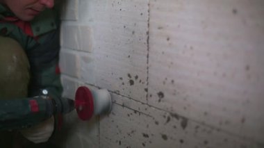 Drilling holes in the wall of a porous block for electrical power socket. Installation of electrical wiring in the house by a man with a puncher