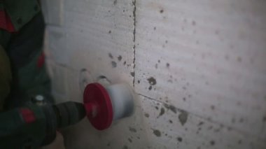 Drilling holes in the wall of a porous block for electrical power socket. Installation of electrical wiring in the house by a man with a puncher