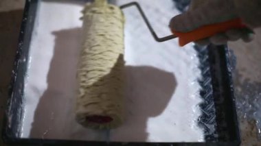 Applying a primer from the tray to the roller, evenly wetting and removing liquid residues. Primer for painting, treatment with dry building mixes. Renovation and finishing of a room in the house