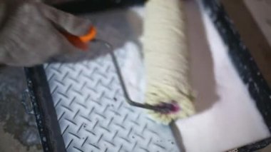 Applying a primer from the tray to the roller, evenly wetting and removing liquid residues. Primer for painting, treatment with dry building mixes. Renovation and finishing of a room in the house