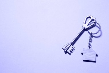 Key chain in the shape of wooden house with key on a purple background. Very peri tinting. Building, design, project, moving to new home, mortgage, rent and purchase real estate. Copy space