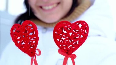 Kalp şeklinde dekorasyonu olan mutlu bir kadın kışın açık havada gözlerinde gözlük ve şapkası olan sıcak beyaz bir kadın. Sevgililer Günü, aşk ve tutku, neşe, aşk ilanı için sevgililer günü kartı, yaşam tarzı
