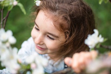 Baharda çiçek açan beyaz bir elma bahçesinde 5 yaşında tatlı küçük bir kız. Bahar zamanı, meyve bahçesi, çiçek, alerji, bahar kokusu, şefkat, doğayla ilgilenme. Portre