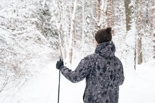 雪に覆われた森を背景に 手にスキーポールを背負ったまま帽子をかぶったスキーヤー 冬の森 アウトドアスポーツ 健康的なライフスタイルのクロスカントリースキー ロイヤリティフリーのストック画像