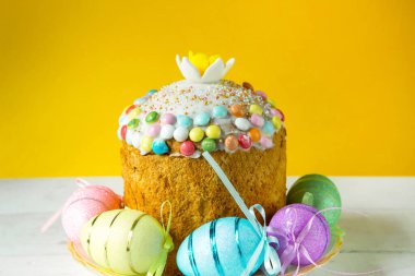 Paskalya pastası, beyaz bir masada boyanmış yumurtalar. Geleneksel bayram yemekleri. Sarı arkaplan