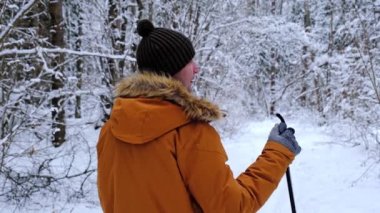 Şapkalı kayakçı, elinde kayak sopalarıyla, karlı ormanda kar altında. Kır ormanlarında kayak yapmak, açık hava sporları, sağlıklı yaşam tarzı. Yavaş çekim 4k video