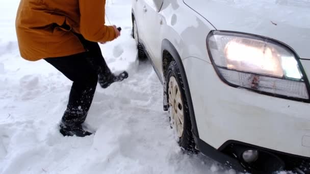 男は車のシャベルで雪の中で車を立ち往生掘ります 冬の交通機関は雪の後 雪のドリフトで立ち往生し 下に座っていた 応急処置 牽引トラック 冬用タイヤスパイクとオールシーズン スローモーション — ストック動画