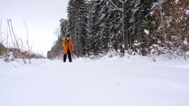 Şapkalı kayakçı, elinde kayak sopalarıyla, karlı ormanda kar altında. Kır ormanlarında kayak yapmak, açık hava sporları, sağlıklı yaşam tarzı. Yavaş çekim 4k video