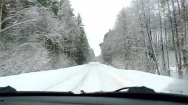 Karla kaplı dar bir otoyol kışın bir çam ormanında, kar yağarken. Arabanın içinden, ön cama kar yağıyor, silecekler çalışıyor. Mevsimlik sürüş güvenliği. Yavaş Hareket