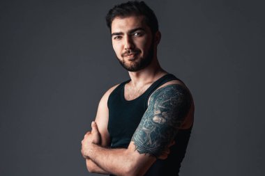 Siyah arka planda dövmesi olan kendine güvenen bir adam. Genç mutlu esmer adam stüdyoda