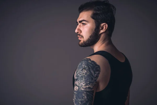 Profile of handsome guy with tattoo in studio. Caucasian strong man on black background