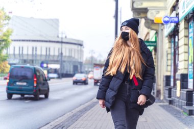 POLAND, BYDGOSZCZ - 12 Kasım 2020: Koruyucu maskeli kız trafiğin yakınında yürüyor. Gündelik tarzda genç bir kadın. Vatandaş