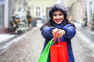Beautiful smiling girl in snowy winter. Happy woman showing shopping bags. Christmas discounts, sale, presents