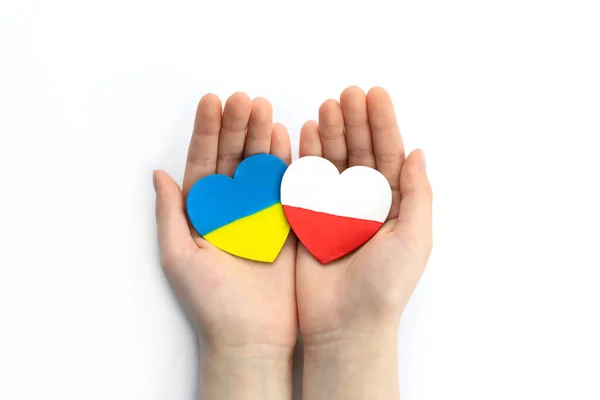 Children\'s hands hold two hearts with flags of ukraine and poland on white background. Unity solidarity help concept