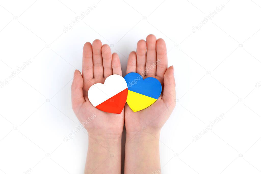 Children's hands hold two hearts with flags of Poland and Ukraine on white background. Unity solidarity help concept
