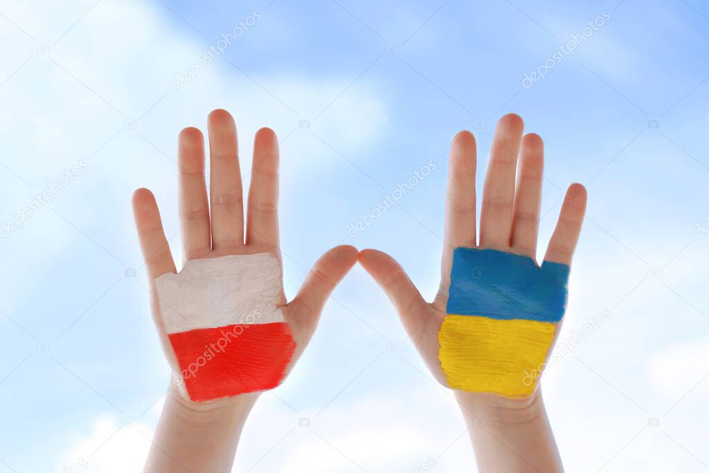 Flags of Poland and Ukraine. Two painted children's palms against blue sky. Unity solidarity help concept