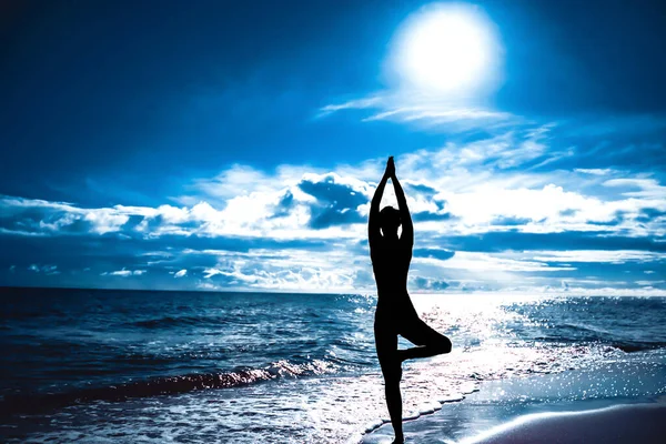 Ağaçta yoga yapan kadın silueti. Güneş gökyüzü ve deniz. Sakinlik ve uyum kavramı. Mavi arkaplan