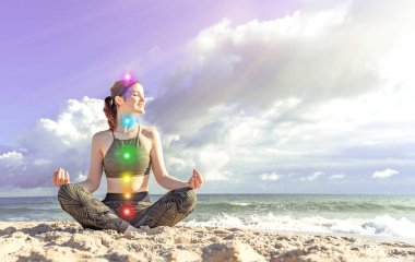 7 çakra. Mutlu kadın deniz kıyısında meditasyon yapıyor. Lotus pozisyonundaki kız