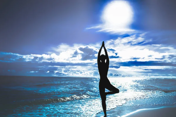 Silhouette of woman in tree pose of yoga. Sun sky and sea. Concept of calm and harmony. Blue background