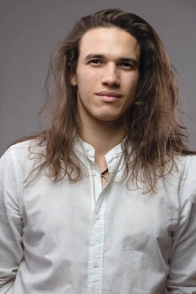 Handsome calm man. Portrait of a young muscular guy with long hair. Strong boy on an isolated grey background in the studio