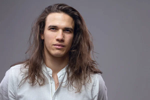 Handsome calm man. Portrait of a young muscular guy with long hair. Strong boy on an isolated grey background in the studio