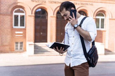 Young man in white shirt talking on phone outdoors. Businessman or student on background of city