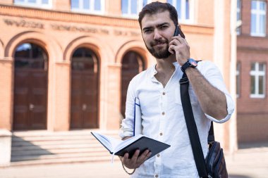 Young handsome business man in white shirt talking on phone outdoors. Self employed. Professional