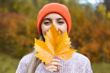 Happy girl with yellow maple leaf. Smiling young woman in autumn park. Portrait