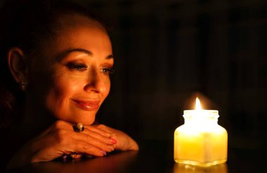 Beautiful adult woman looks at fire of candle. Portrait of a pensive girl. Concept