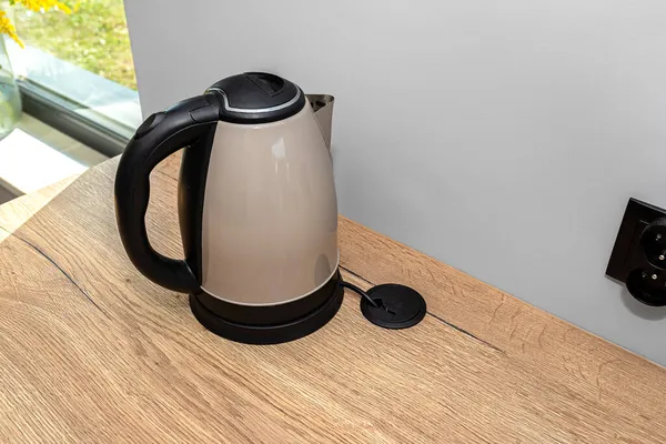 An electric kettle standing on the countertop on the kitchen cabinets, visible hole in the table top through which the electric cable goes.