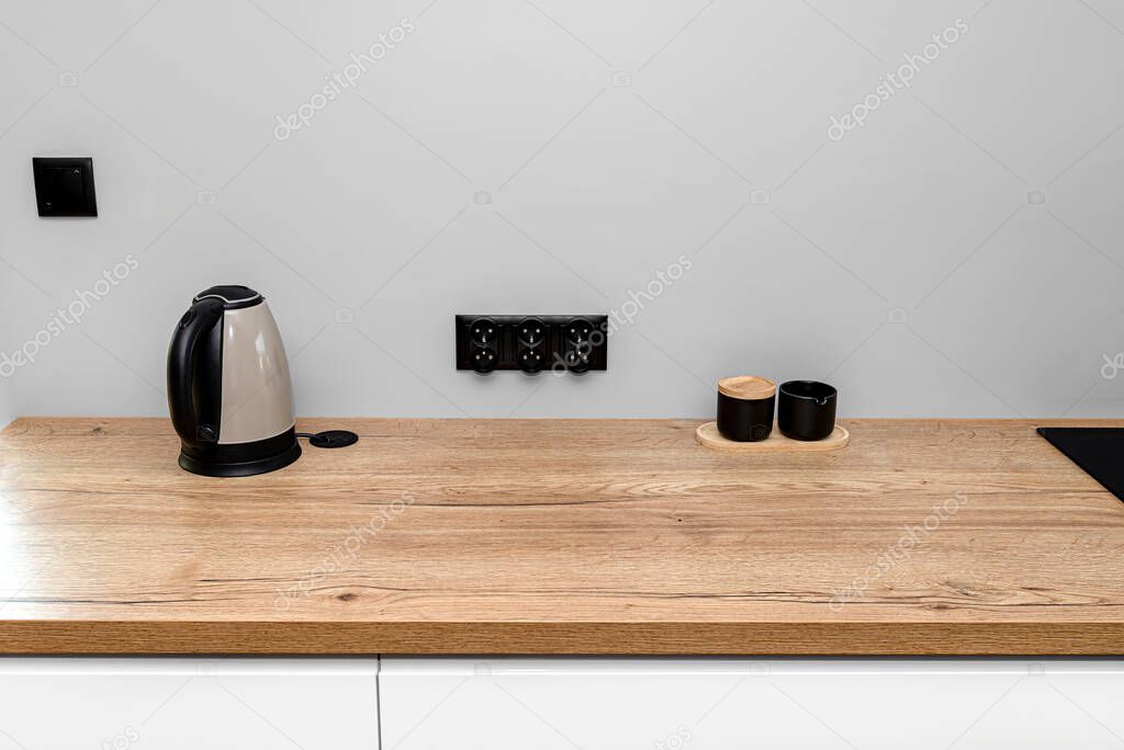 An electric kettle standing on the countertop on the kitchen cabinets visible sugar bowl and milk container.