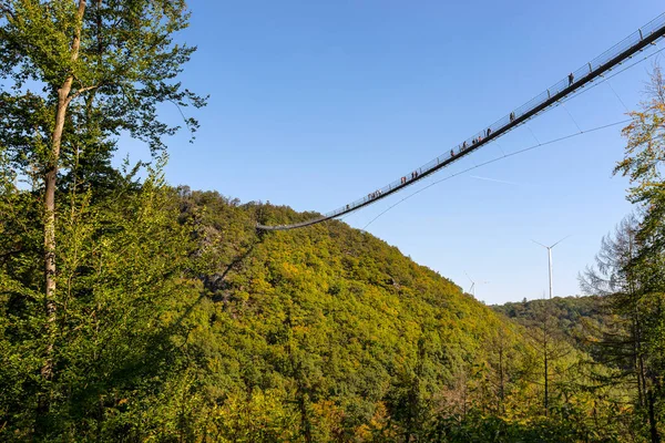 一座挂着钢绳的木制桥 在蓝天的映衬下俯瞰着 桥上可见的游客和风力涡轮机 — 图库照片