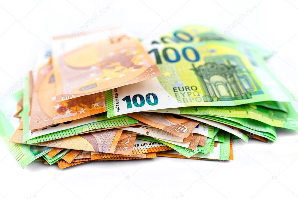 Macro photo of European Union currency, scattered on pile of 50 and 100 euro banknotes, isolated on a white background.
