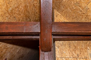 Çatı kirişleri tavan arasında görünür, tahtada görünür çatlaklar ve OSB tahtalarıyla kaplı duvarlarla kahverengi boyanmış..