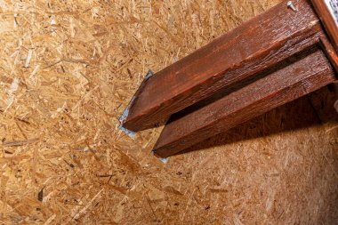 Çatı kirişleri tavan arasında görünür, tahtada görünür çatlaklar ve OSB tahtalarıyla kaplı duvarlarla kahverengi boyanmış..