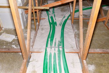 Pipe insulation with expanded perlite in domestic ventilation with energy recovery, a visible system of green pipes spread over the roof trusses.