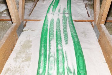 Pipe insulation with expanded perlite in domestic ventilation with energy recovery, a visible system of green pipes spread over the roof trusses.