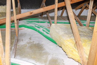 Expanded perlite and mineral wool insulation laid on pipes in domestic ventilation with heat recovery, green pipes laid on the roof truss.
