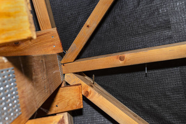 Badly nailed nails connecting the roof truss covered with a membrane on a single-family house, damaged truss visible.