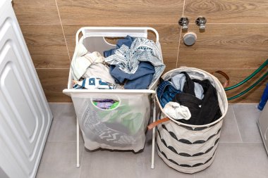 Kazan dairesinde kirli çamaşırlı iki kumaş sepet, çamaşır makinesinin yanında duruyor..