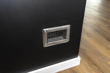 Condensate tank behind the grille in a modern fireplace with a closed combustion chamber standing in the living room in black. clipart