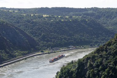Loreley, Almanya - 25 Temmuz 2021. Batı Almanya 'da Ren Nehri' nde bir sürü konteynır taşıyan büyük bir mavna, ağaçlarla kaplı görünen tepeler..