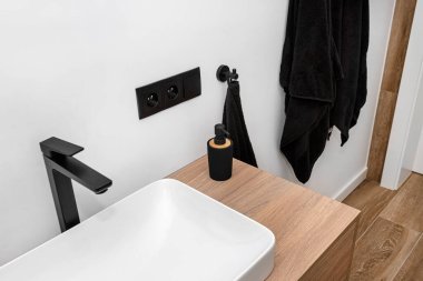 Banyoda modern bir lavabo, siyah bir tıkırtı, zemin ahşabı taklit eden seramik fayanslarla kaplı..