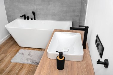 Banyoda modern bir lavabo. Duvara monte edilmiş siyah bir musluk. Gri seramik fayanslarla kaplı bir duvar..