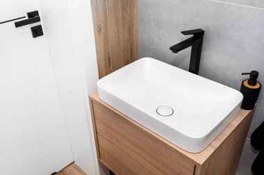 Tuvalette modern bir lavabo. Duvara monte edilmiş siyah bir musluk. Gri seramik fayanslarla kaplı bir duvar..
