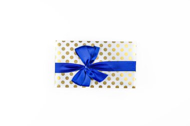 A gift wrapped in white paper with gold circles wrapped in a blue ribbon tied in a bow, isolated on a white background, top view.